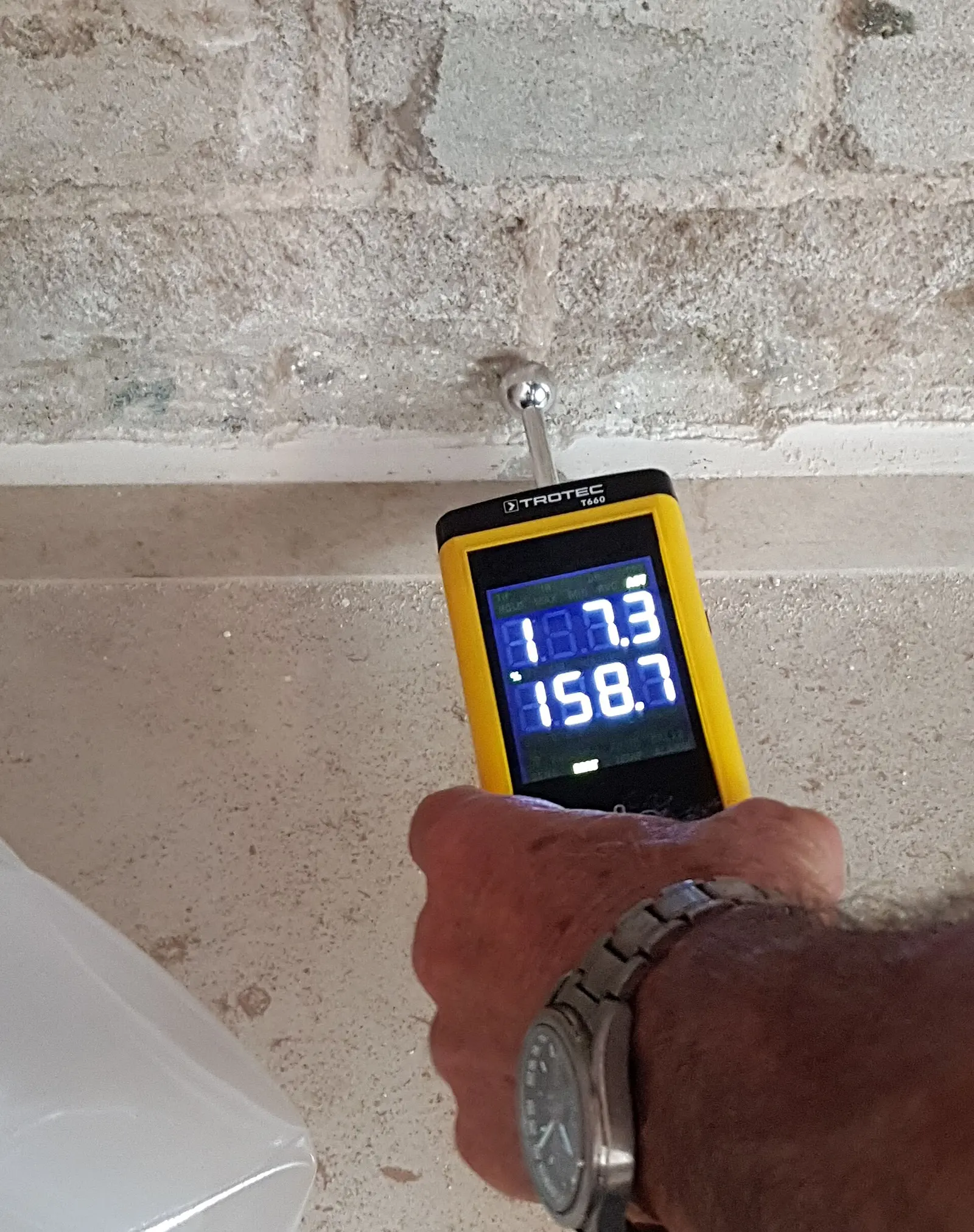 A pin moisture meter held against a masonry wall. Shown on the Attic mold page for Cape Coral, FL.